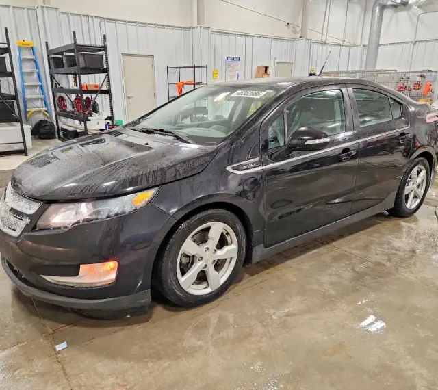 Czarny Chevrolet Volt stoi w garażu, mokry od deszczu. W tle regały z narzędziami i drabina.