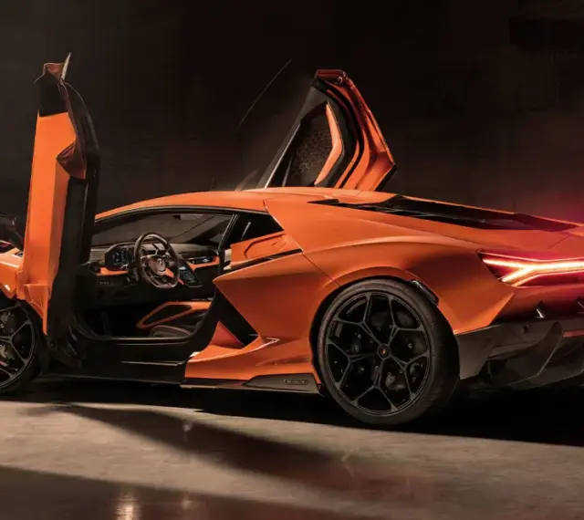 Pomarańczowy Lamborghini Revuelto z otwartymi drzwiami, ukazujący sportowe wnętrze i agresywną sylwetkę.