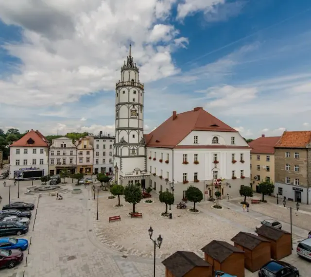 Rynek w Paczkowie, polskie Carcassonne, z ratuszem i wieżą. Brukowany plac, samochody, ławki i małe drewniane budki.