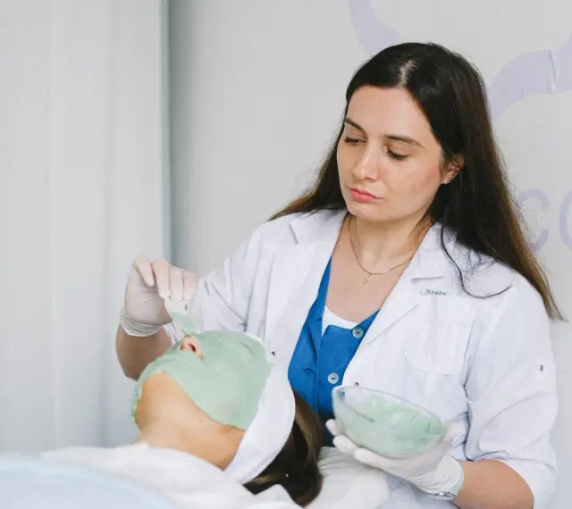 Dermatolog nakłada zieloną maskę na twarz pacjentki.