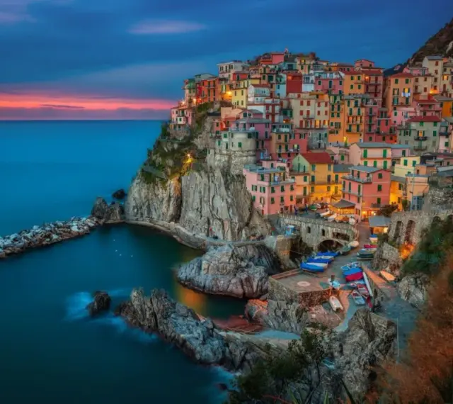Kolorowe domy Cinque Terre, jedne z najpiękniejszych regionów Włoch, wznoszą się na klifie nad morzem o zachodzie słońca.