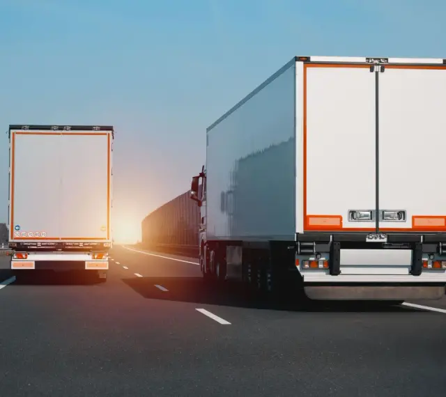 Dwa białe tiry jadą autostradą. Na jednym z nich widać znak zakazu wyprzedzania dla ciężarówek.