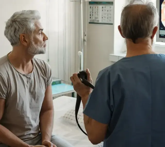 Lekarz wykonuje rektoskopię u pacjenta, obserwując obraz na monitorze.