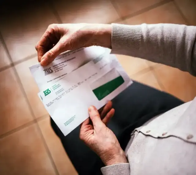 Dłonie trzymają kopertę ZUS. W środku dokumenty dotyczące 13 emerytury netto.
