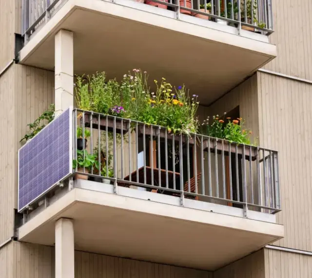Po wypadkach, kto kontroluje stan techniczny balkonów w starych blokach? Ten balkon z panelami słonecznymi i kwiatami wygląda na zadbany.
