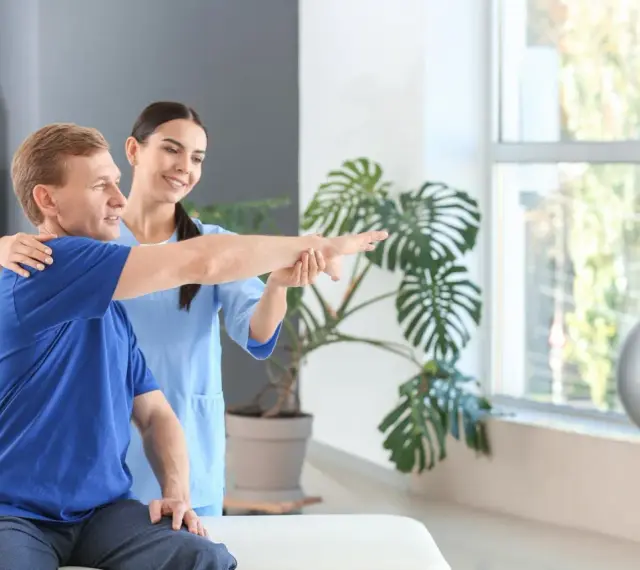 Ein Physiotherapeut unterstützt einen Patienten bei der Armbewegung.