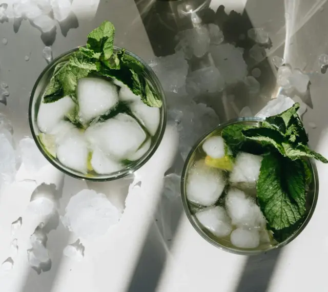Dwa orzeźwiające mojito z lodem i miętą, otoczone pokruszonym lodem, w letnim słońcu.