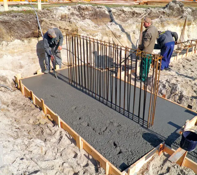 Budowa fundamentów: pracownicy wylewają beton, przygotowując zbrojenie pod przyszły żelbeton.