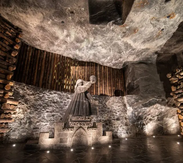 Kopalnia soli Wieliczka ciekawostki: rzeźba górnika Mikołaja Kopernika w solnej komorze, otoczona drewnianymi belkami i solnymi ścianami.