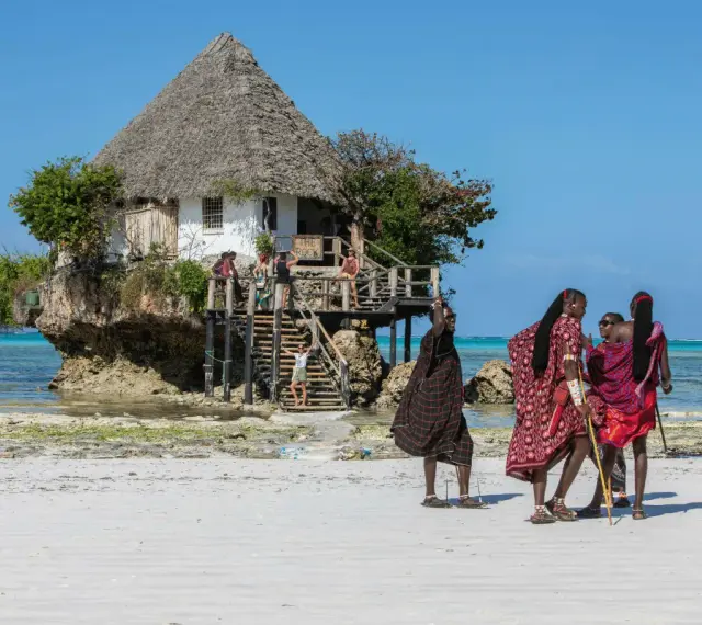 Wspaniały marzec na Zanzibarze. Ludzie w tradycyjnych strojach spacerują po plaży przy restauracji "The Rock" na skale.