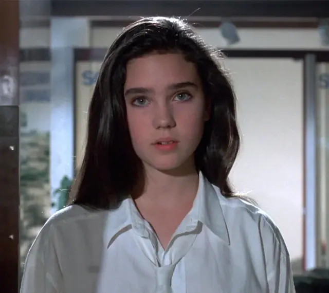Młoda Jennifer Connelly w białej koszuli, z charakterystycznym spojrzeniem, jak z jej wczesnych filmów.