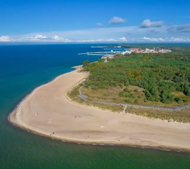 Widok z lotu ptaka na piaszczystą plażę, las i miasteczko na Półwyspie Helskim.