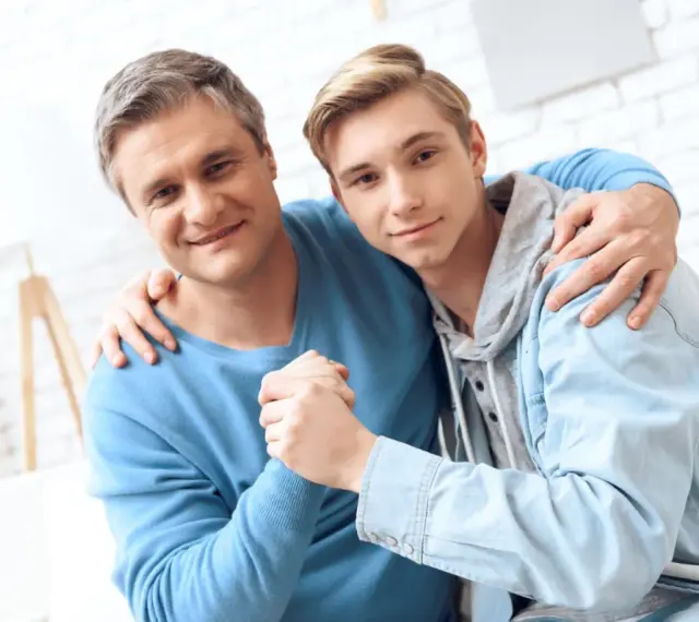Ojciec obejmuje syna, wspierając go w ważnych życiowych rozmowach.