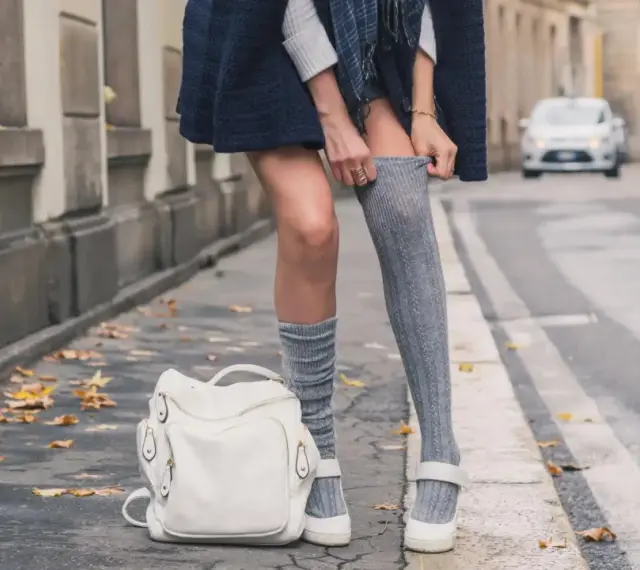 Stylizacja z długimi skarpetkami damskimi, biały plecak i jesienne liście na chodniku.