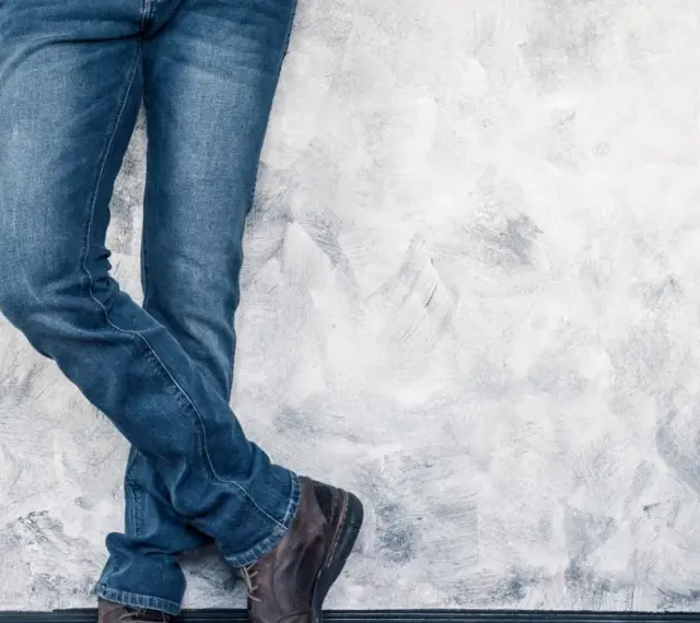 Mężczyzna w jeansach H&M, stojący przy ścianie. Rozmiarówka H&M wypada standardowo, idealnie dopasowana.