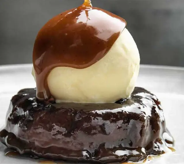 En läcker sticky toffee pudding med en kula vaniljglass och varm kolasås som rinner över.