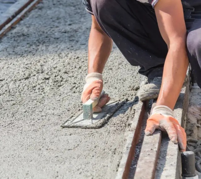 Pracownik wygładza świeży beton, dbając o odpowiednie suchy beton proporcje. Ręce w rękawiczkach trzymają kielnię.