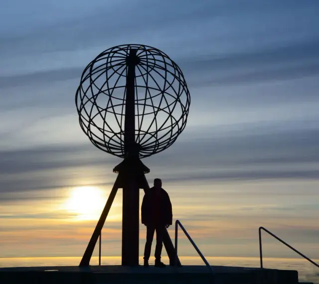Sylwetka człowieka przy globusie na Nordkapp podczas zachodu słońca.
