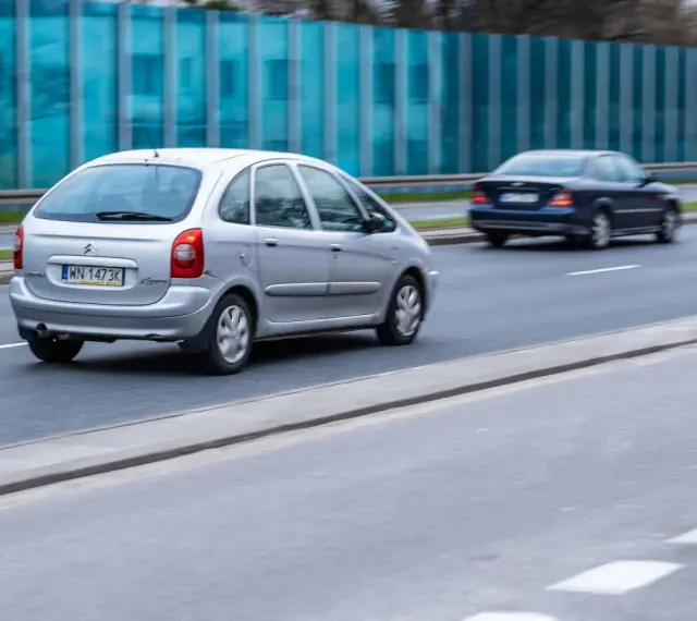 Srebrny Citroën Xsara Picasso jedzie po drodze, mijając inne samochody.