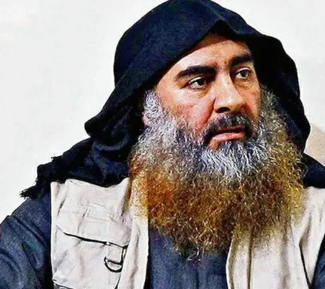 Mężczyzna z długą, siwiejącą brodą i czarnym nakryciem głowy, przypominający Abu Bakra al-Baghdadiego, siedzi w jasnym ubraniu.