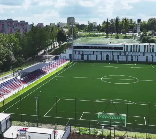 Nowy stadion Polonii Bytom z zieloną murawą, trybunami w kolorach czerwonym i niebieskim oraz nowoczesnym budynkiem klubowym.
