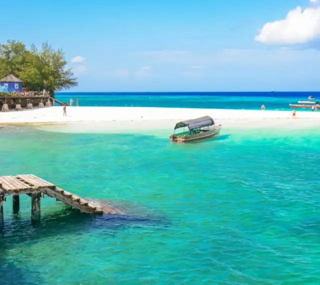 Zanzibar - wczasy opinie: turkusowa woda, biała plaża, drewniany pomost i łodzie. Rajskie widoki idealne na wakacje.