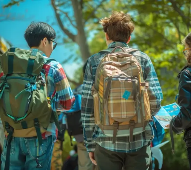 Trois jeunes avec des sacs à dos près d'un bus, prêts pour leur voyage scolaire. L'aide financière pour voyage scolaire rend ces aventures possibles.