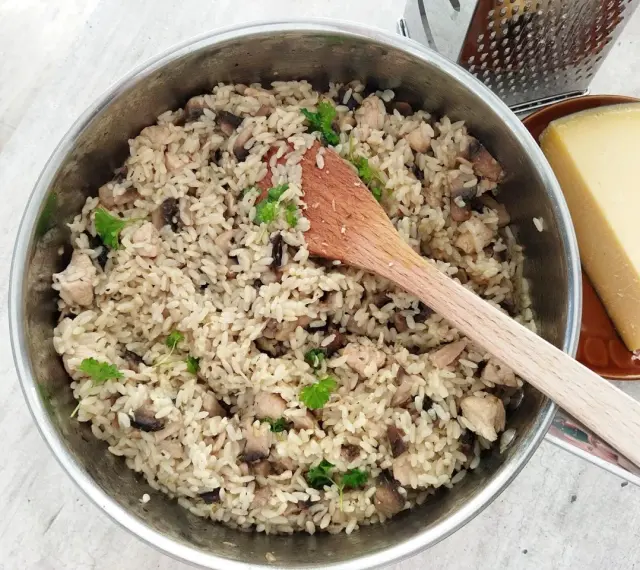 Kremowe risotto z pieczarkami i kurczakiem w garnku, obok kawałek parmezanu i tarka.