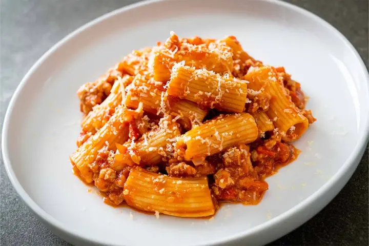 Un piatto invitante di pasta alla zozzona, con rigatoni conditi con un ricco ragù e abbondante parmigiano grattugiato.
