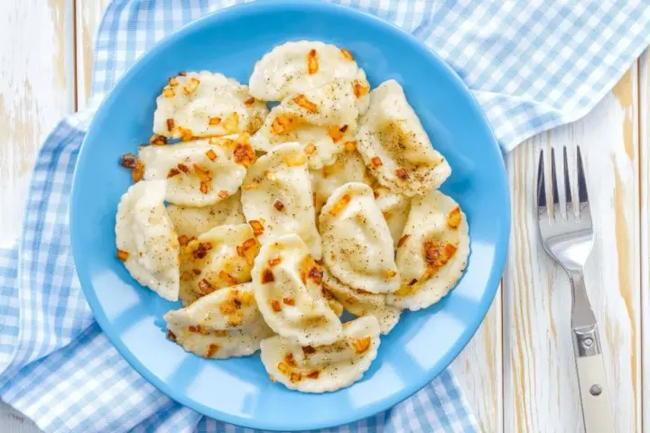 Pyszne pierogi z soczewicą czerwoną, posypane skwarkami i pieprzem, na niebieskim talerzu.