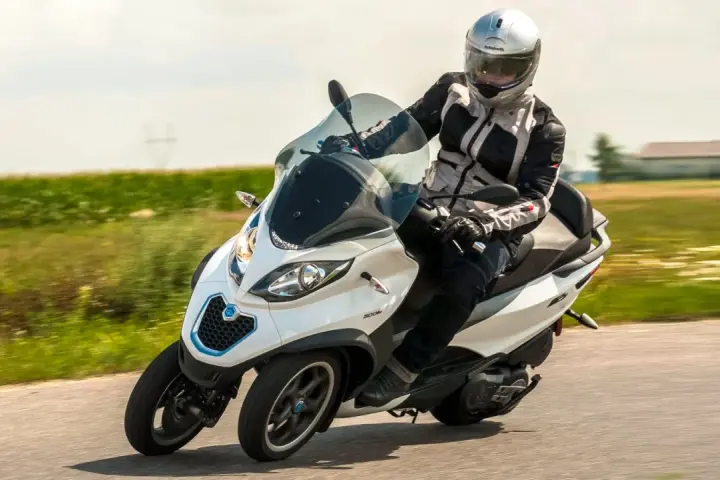 Biały Piaggio MP3 500 z kierowcą w kasku pędzi po drodze. Zastanawiasz się nad jego spalaniem?