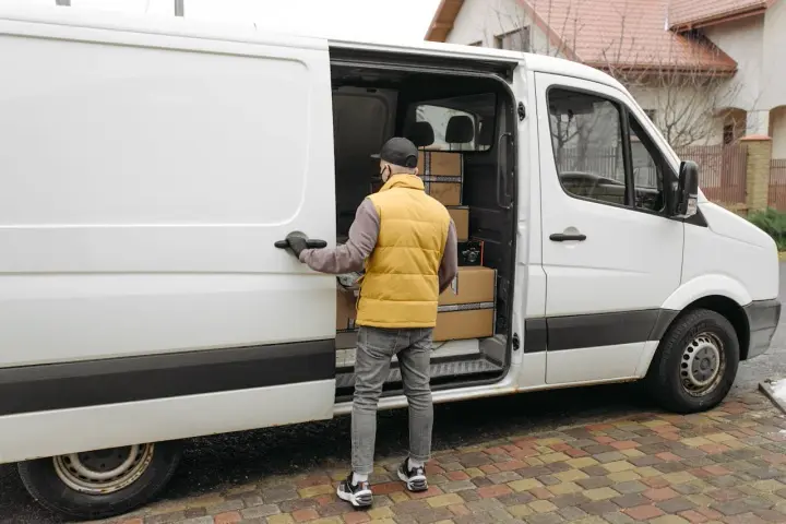 Kurier otwiera drzwi białego busa dostawczego, w którym widać paczki. Zastanawiasz się, ile waży bus dostawczy?