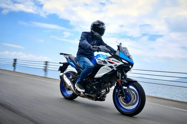 Motocyklista na niebiesko-białym Suzuki SV650X, idealnym motocyklu do 35kW, jedzie wzdłuż wybrzeża.