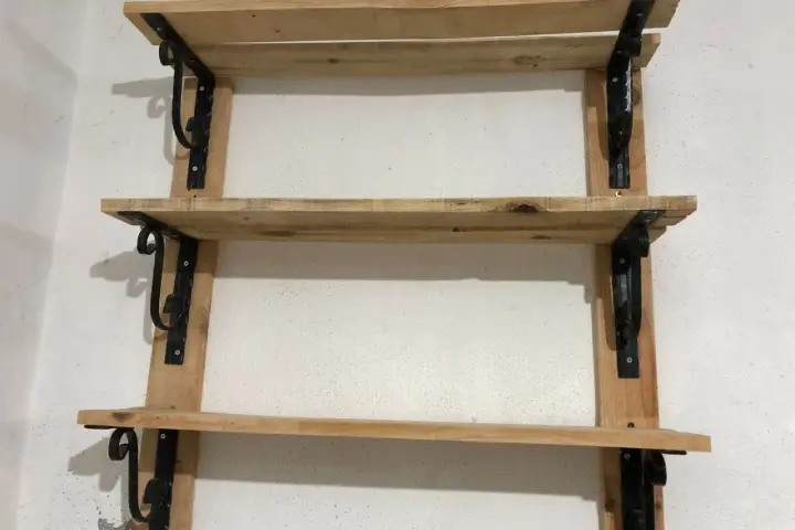 Scaffali fai da te garage: tre ripiani in legno grezzo, fissati a parete con staffe nere decorative. Perfetti per organizzare attrezzi e materiali.