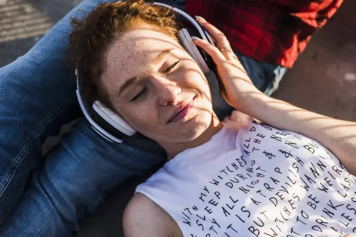 Jeune femme aux taches de rousseur, écouteurs blancs, profitant de la musique. Le volume est à 95 db équivalent, elle semble détendue.
