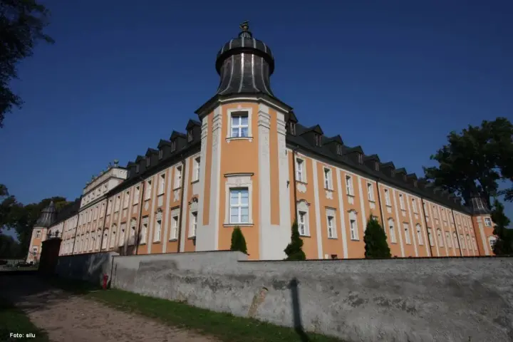 Klasztor Paradyż, okazały budynek z pomarańczowo-białą fasadą i wieżyczką, otoczony murem.