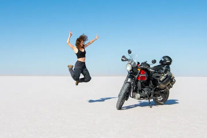 Donna salta di gioia su un deserto di sale, moto pronta per l'avventura. Questo è cosa significa on the road: libertà e scoperta.