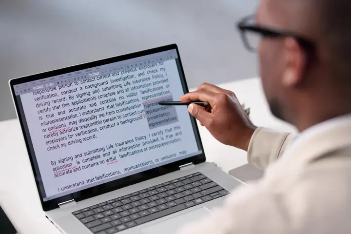Un homme examine un document sur un écran d'ordinateur, soulignant des passages pour apprendre comment reconnaître une pièce fautée.
