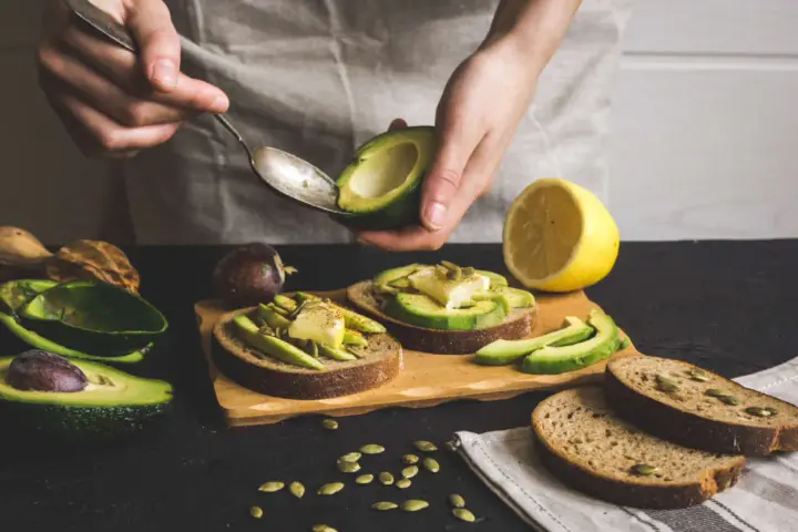 Preparazione di gustose ricette con avocado: toast con avocado, formaggio e semi.