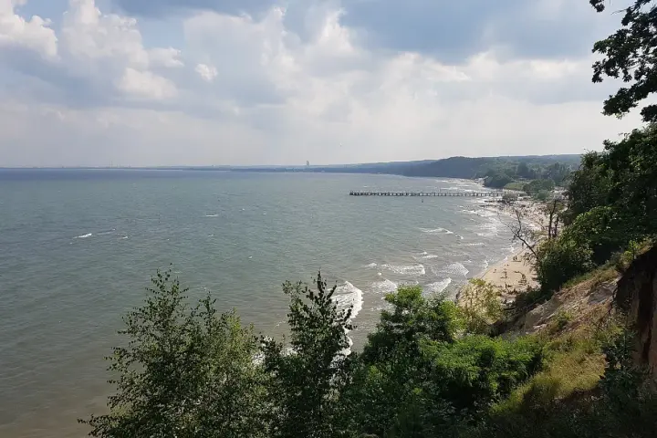 Widok z klifu orłowskiego na morze, plażę z ludźmi i molo. W oddali widać zarys wybrzeża.