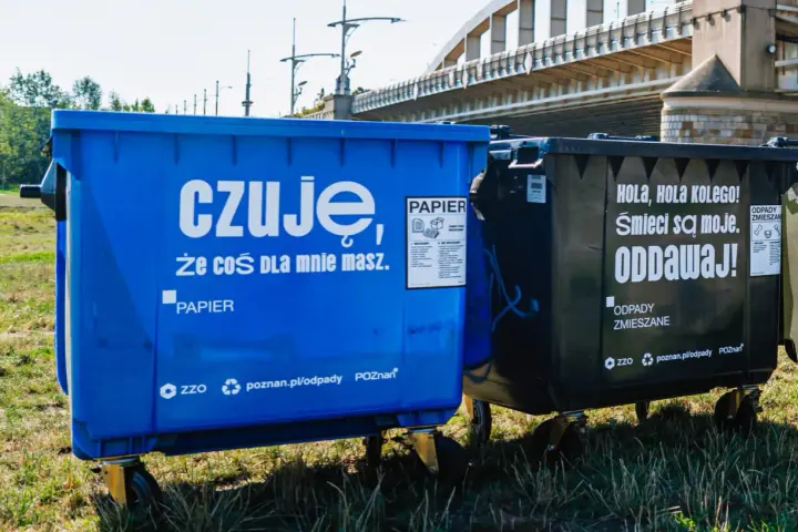 Niebieski kontener na makulaturę z napisem "czuję, że coś dla mnie masz. PAPIER" obok czarnego na odpady zmieszane.