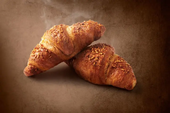 Dwa chrupiące croissanty posypane orzechami. Pyszna przekąska, ale warto pamiętać o ich kaloryczności - croissant kcal.