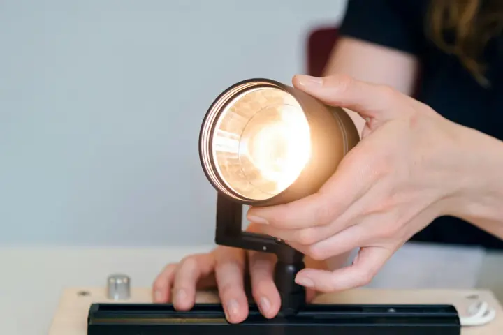 Händer justerar en lampa, kanske för att ta bort dimmer. Ljuset är starkt.