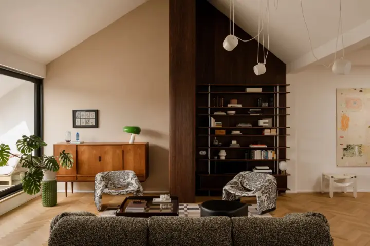 Salón acogedor con **techo inclinado interior**, muebles de madera, estanterías y sillones estampados.