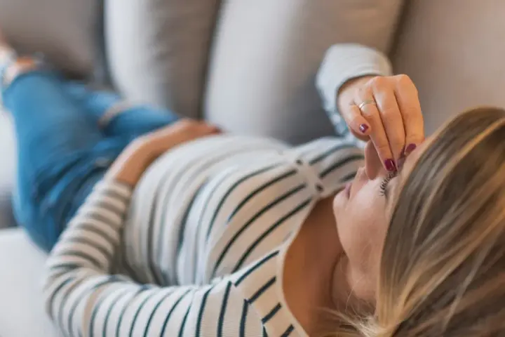 Kobieta w ciąży leży na kanapie, dotykając czoła. Zmartwienie o brak bicia serca w 8 tygodniu ciąży maluje się na jej twarzy.