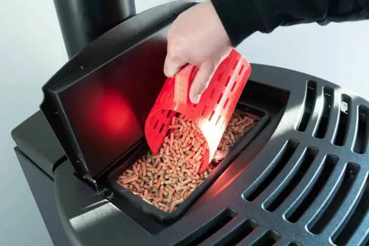 Main d'une personne versant des granulés de bois dans un poêle Palazzetti. Réglage de l'alimentation pour un fonctionnement optimal.