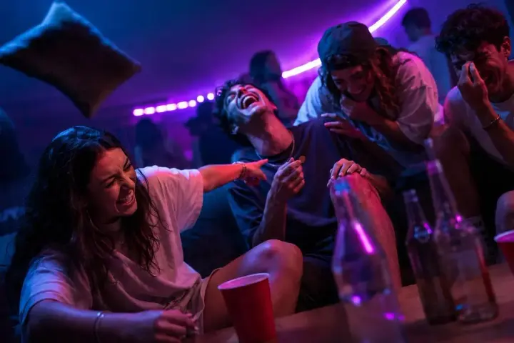 Ungdomar skrattar och har kul på en fest, kanske med kluriga gåtor till festen. Ljusen är lila och blå.