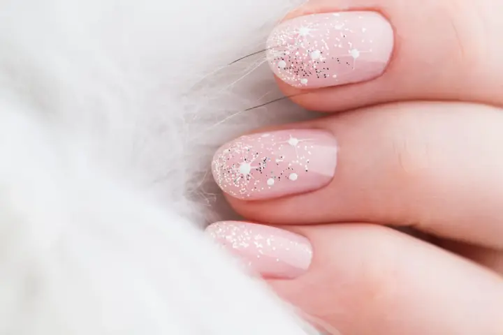 Unghie natalizie rosa pastello con brillantini scintillanti e decorazioni a stella, su sfondo bianco soffice.