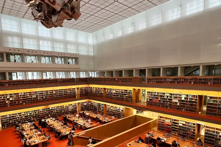 Große Bibliothek mit vielen Regalen voller Bücher. Menschen sitzen an Tischen und lesen. Ein Ort für Lesungen in Berlin.