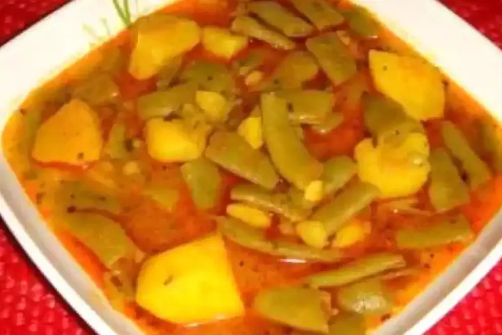 Un plato humeante de judías verdes con patatas, cocinado en una sabrosa salsa rojiza.